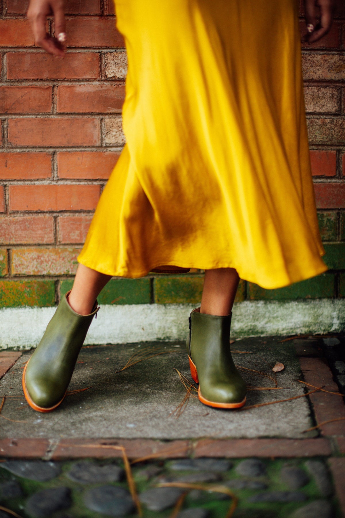 Women's olive green leather ankle boots with tapered heels styled with a flowing yellow dress