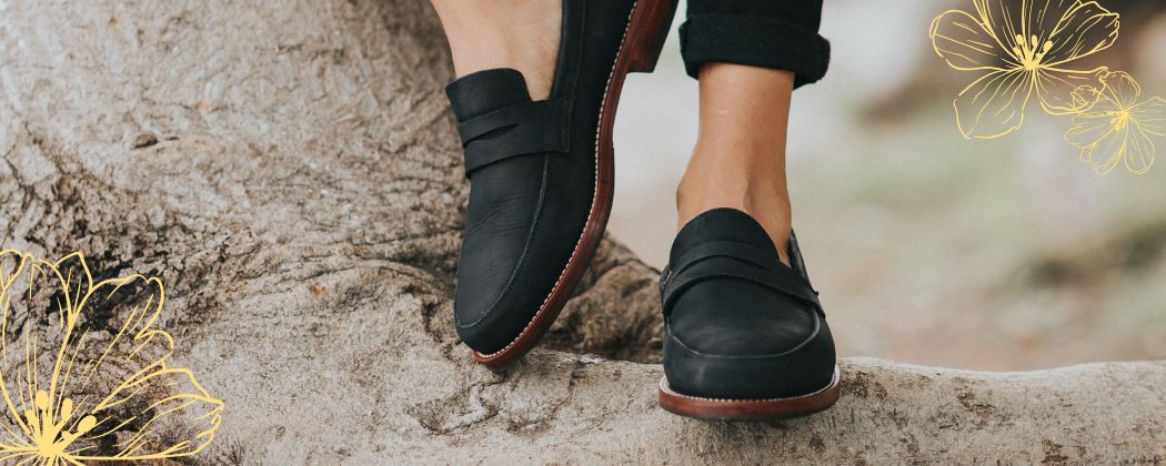 Handcrafted women's black leather penny loafers standing on a natural textured tree root from the Adelante Made-to-Order Women's Shoes & Sandals Collection.