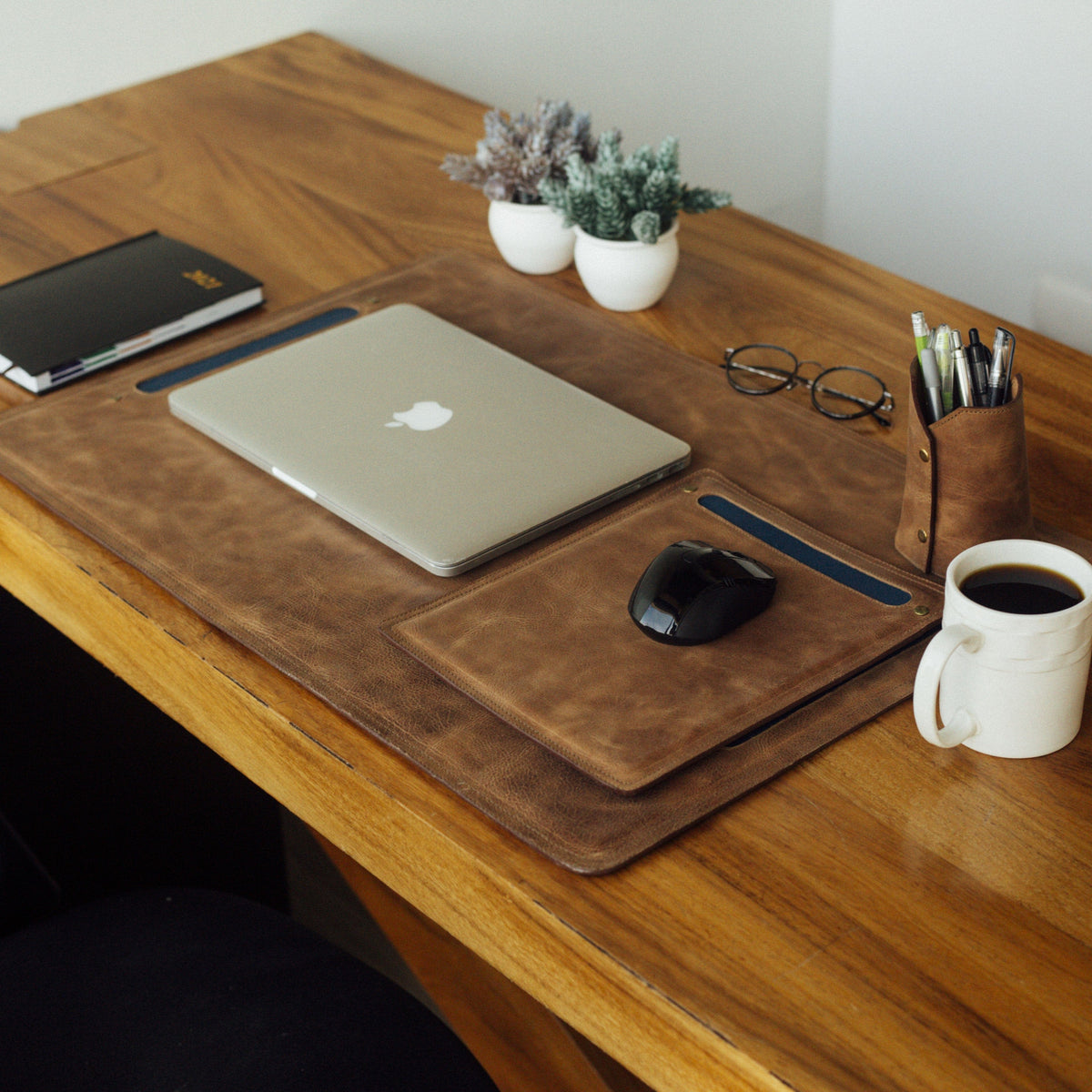 Leather desk mat and mouse pad with laptop coffee cup glasses and pencil holder on a wooden desk