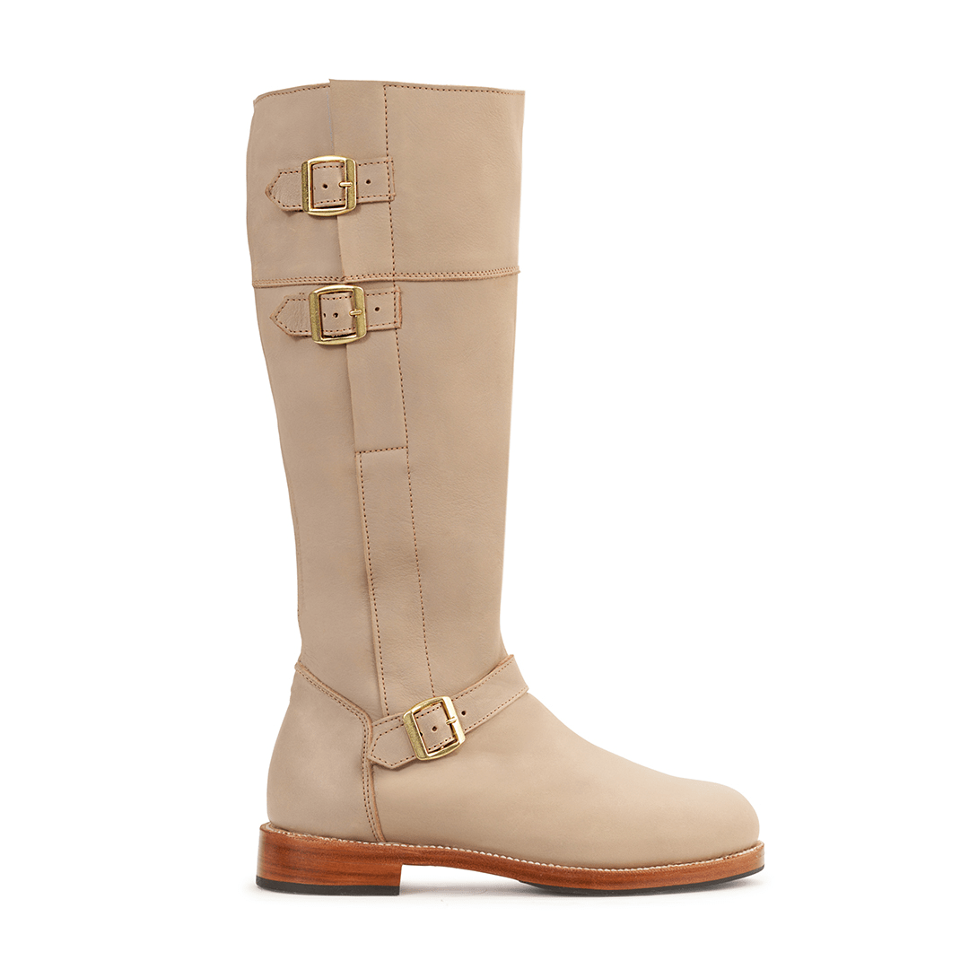 Beige women's knee high riding boot with three brass buckles and wraparound leather detailing, handcrafted to order with wide calf width options by Adelante