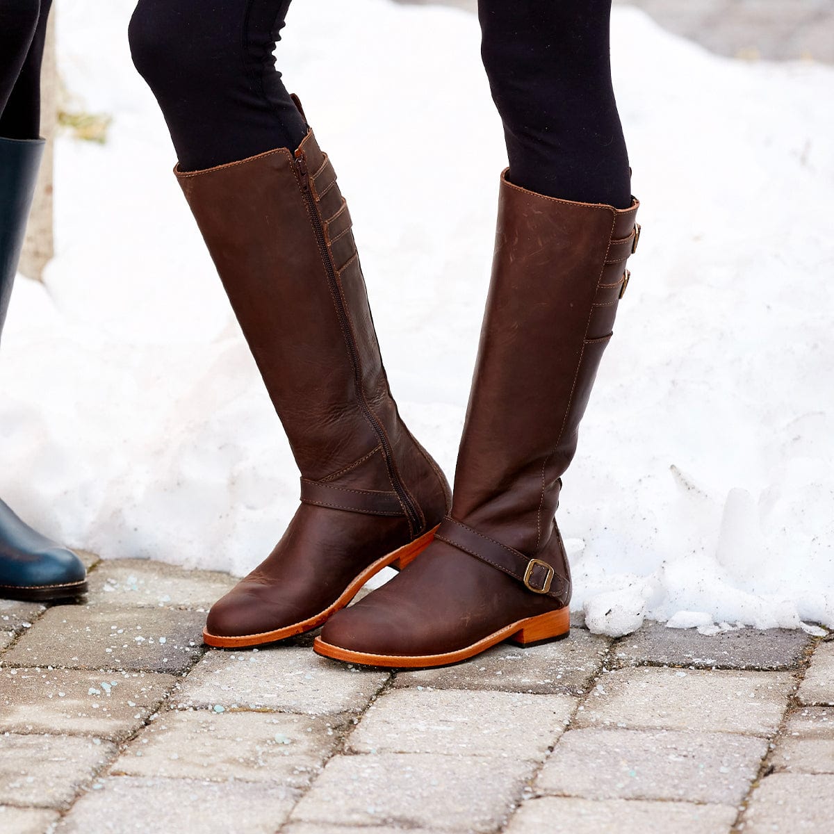 Brown leather women's knee-high riding boots with wraparound buckle detail and wide calf fit, handcrafted by Adelante Made-To-Order