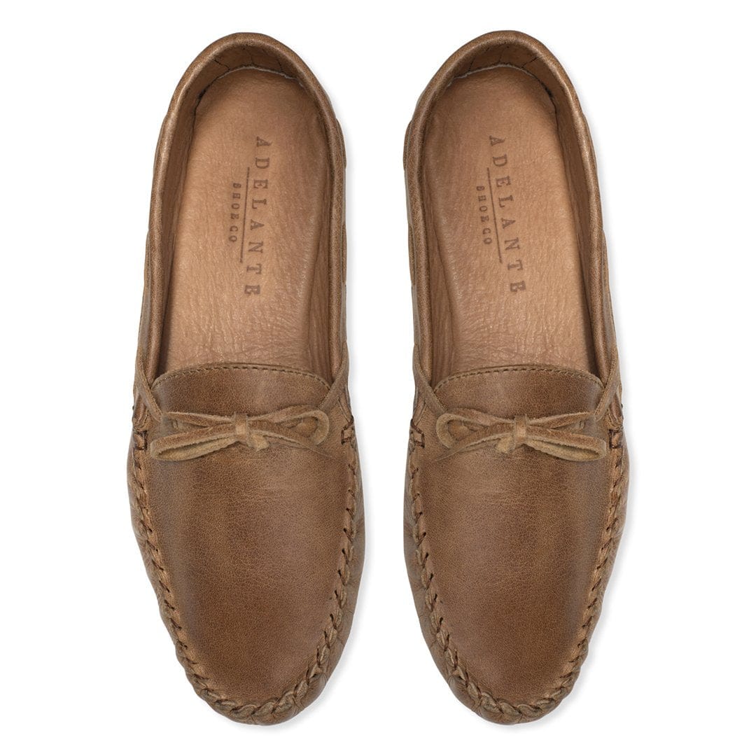 Women's brown leather moccasins with tie bows and braided stitching, handcrafted for comfortable indoor wear