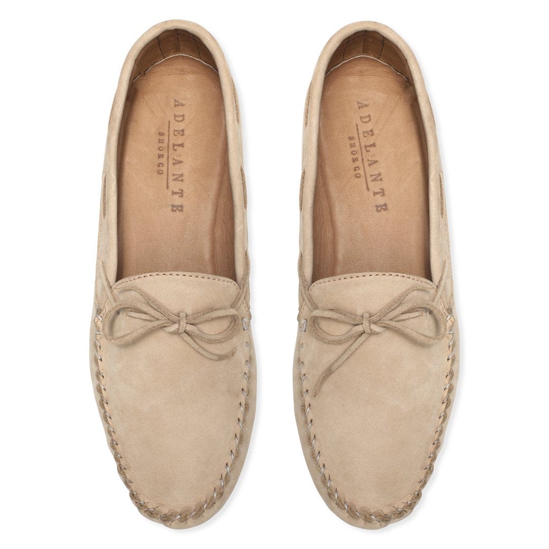 Women's beige nubuck leather moccasins with bow detail and hand-stitched soles, shown as a pair